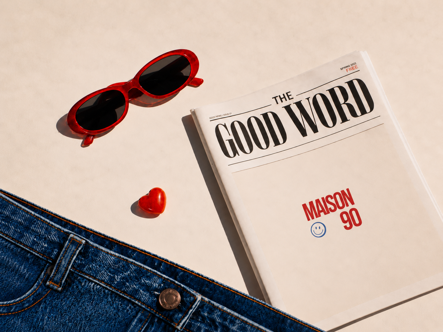 Flat-lay Maison 90 : lunettes rouges, journal THE GOOD WORD, cœur rouge et denim